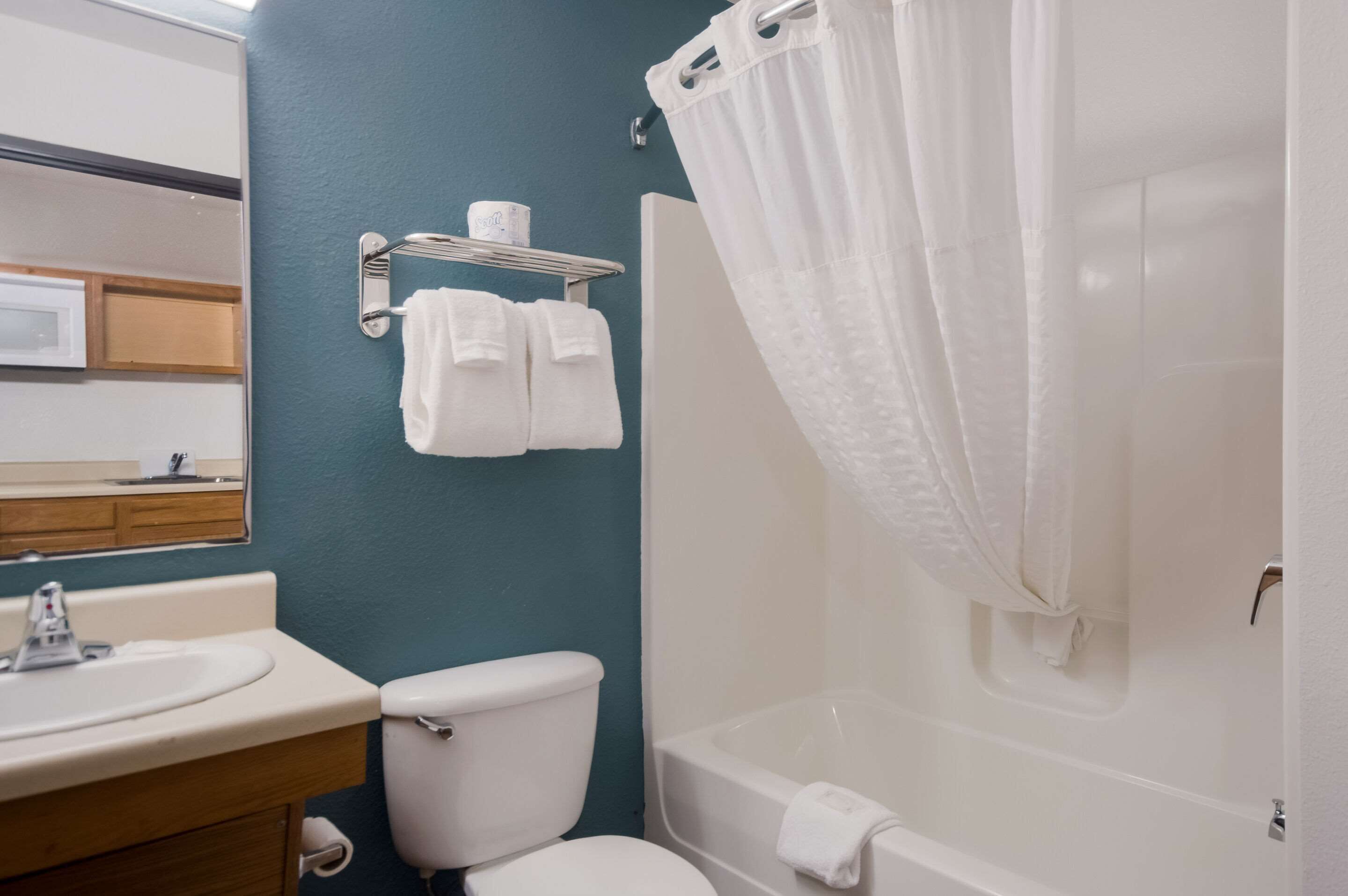A bathroom with a sink, toilet, and bathtub. There is a towel rack with two towels and a roll of toilet paper.