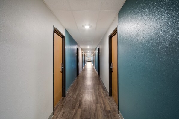 A long, narrow hallway with wooden flooring and doors on both sides. - WoodSpring Suites Augusta Fort Eisenhower (Augusta)