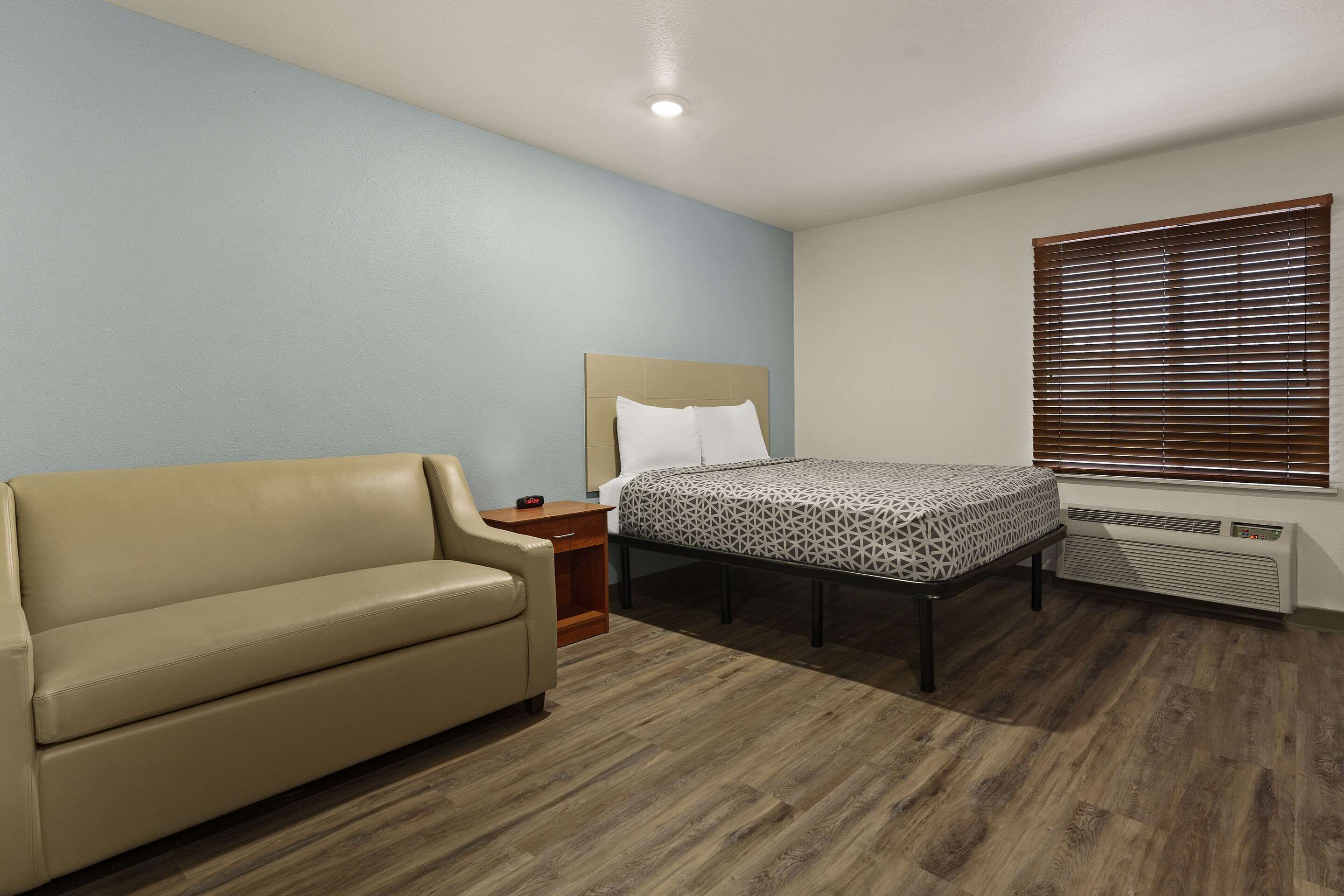 A bedroom with a bed, a sofa, a nightstand, and a window with blinds.