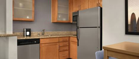 A kitchen with wooden cabinets, a stainless steel refrigerator, a dishwasher, a coffee maker, and a blue chair.