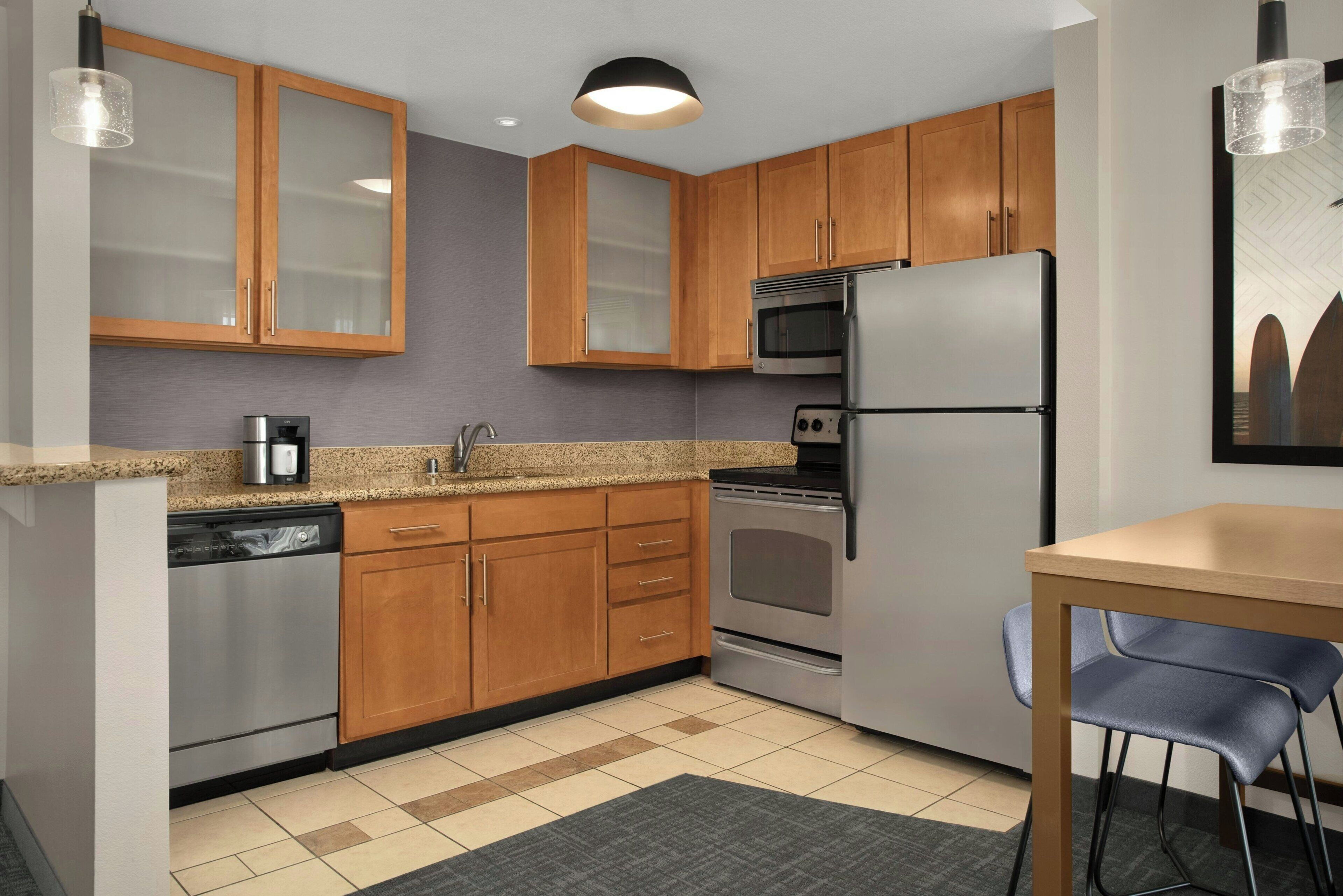 Una cocina moderna con armarios de madera, electrodomésticos de acero inoxidable, lavavajillas y un comedor con mesa y sillas.