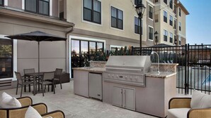 An outdoor kitchen area with a grill, dining table, chairs, and an umbrella. - Residence Inn by Marriott San Diego Oceanside (Oceanside)