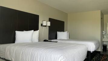 A hotel room with a large bed, a smaller bed, a nightstand, a lamp, and a bathroom visible in the background.