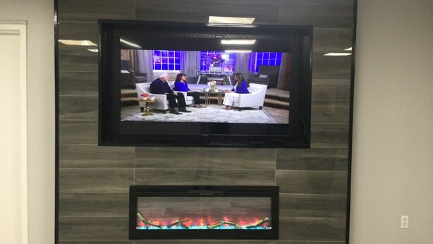 Litteä näyttöinen televisio on kiinnitetty tummaan, laatoitettuun seinään takan yläpuolelle.