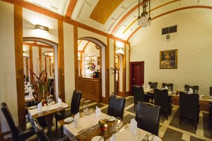 A dining area with tables set for multiple guests, featuring a classic design with wooden chairs and a chandelier.