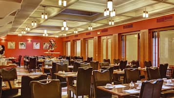 A spacious dining area with multiple tables and chairs, wooden paneling on the walls, and pendant lighting.