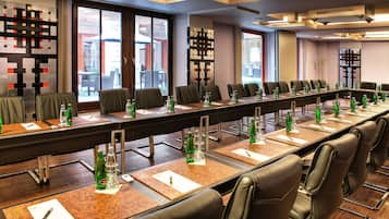 Ein Konferenzraum mit langem Tisch, mehreren Stühlen und verschiedenen Annehmlichkeiten wie Wasserflaschen und Gläsern.