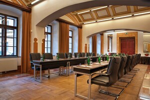 Uma sala de conferências com uma mesa comprida, várias cadeiras e uma porta vermelha ao fundo.