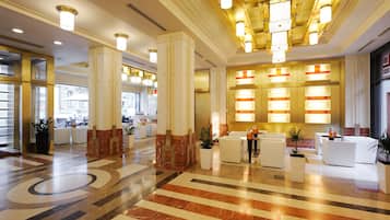 Un hall amplio con suelo de mármol, zona de recepción blanca e iluminación moderna.