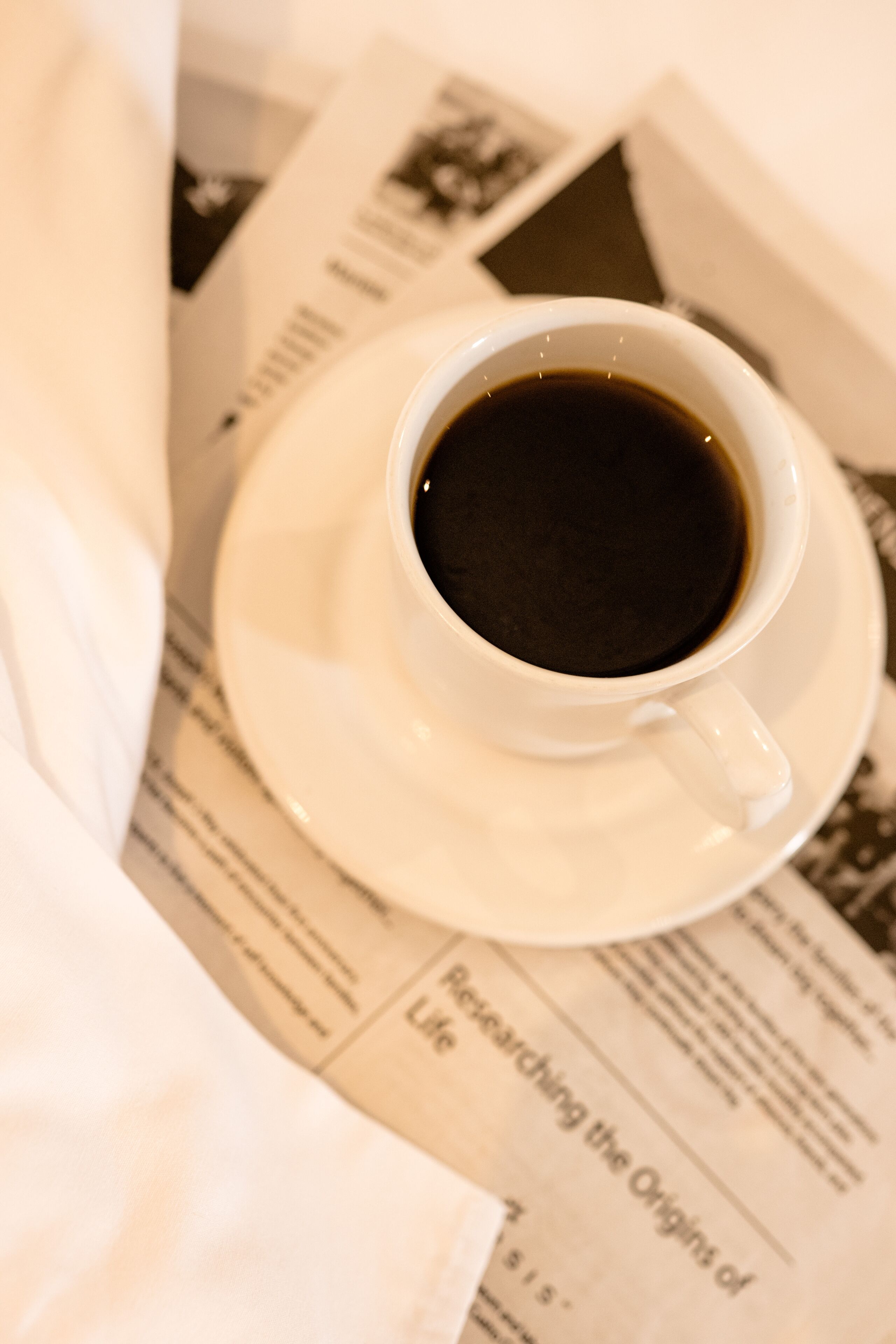 A cup of coffee on a saucer with a newspaper underneath.