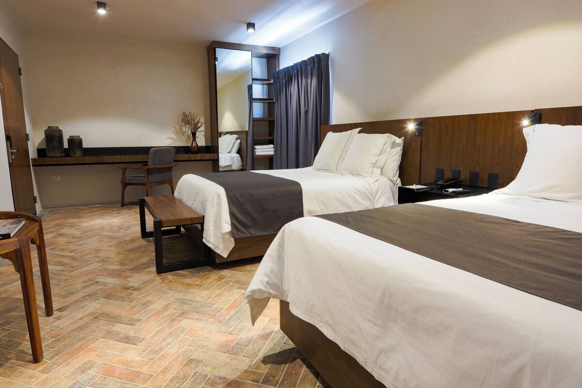 Une chambre d’hôtel avec deux lits, un bureau, une chaise et un miroir.