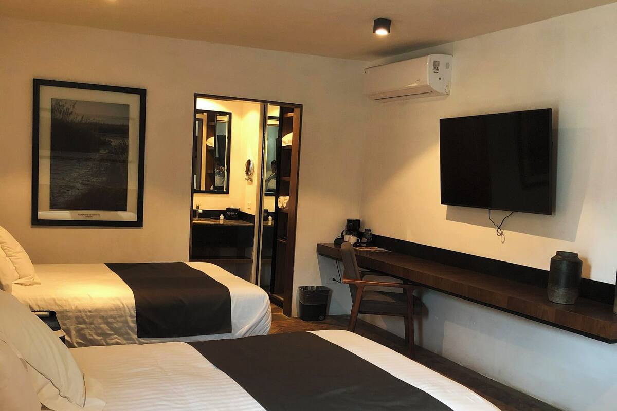 Une chambre d’hôtel avec deux lits, un bureau, une chaise, une télévision et un tableau encadré au mur.