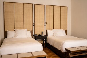 A hotel room with two beds, a wooden bench, a nightstand, and a wall-mounted panel.