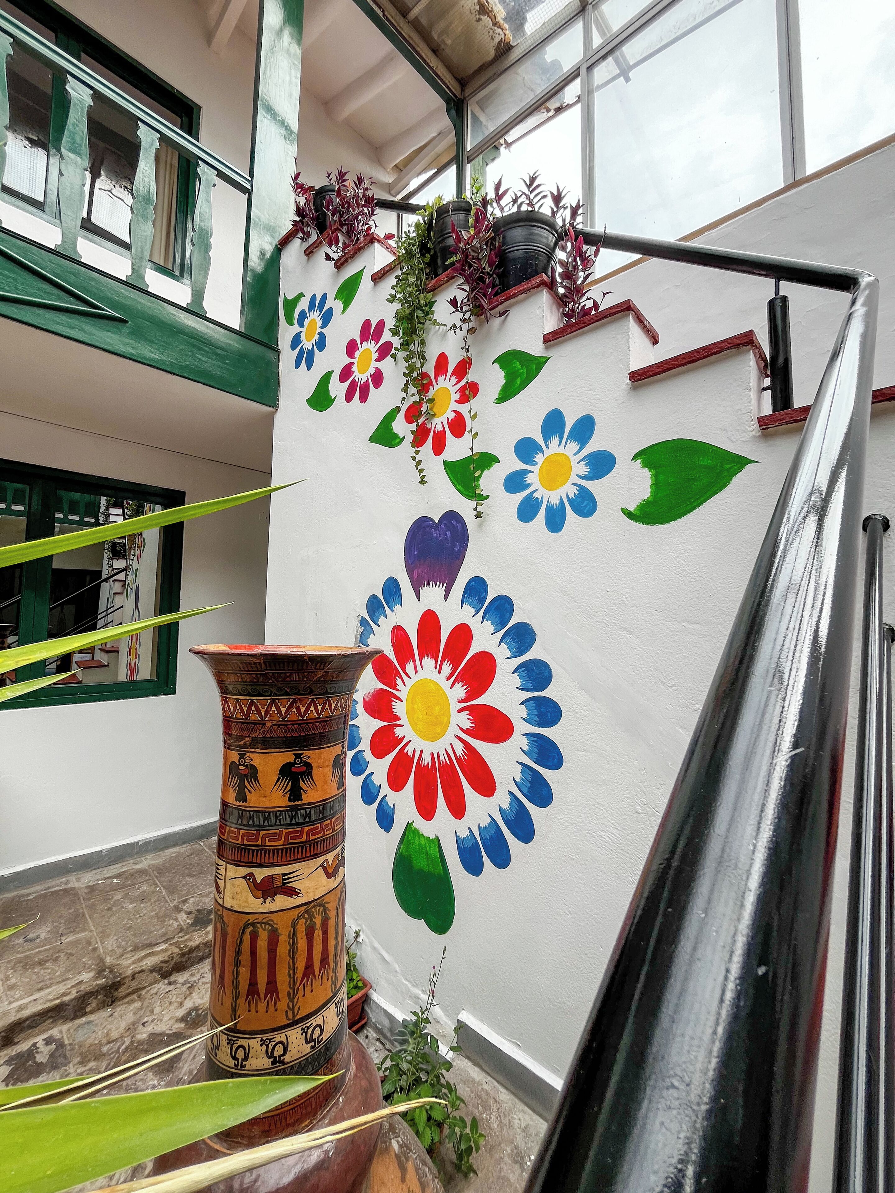 Een gebouw met een witte muur versierd met kleurrijke bloemmotieven en een grote keramieken pot met traditionele patronen.