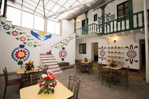 Uma área de refeições com mesas e cadeiras, uma escada e arte decorativa nas paredes.