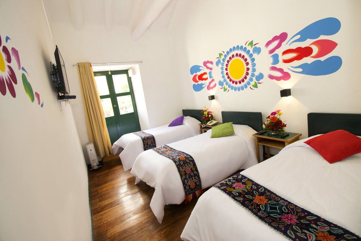 A hotel room with two beds, a wooden floor, a green door, and colorful wall decorations.