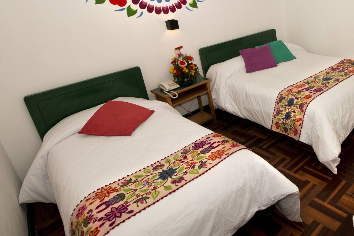 Two single beds with green headboards, white bedding, and colorful embroidered bedspreads.