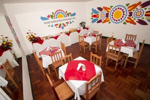 Uma área de refeições com várias mesas e cadeiras, decorada com flores e um mural na parede.