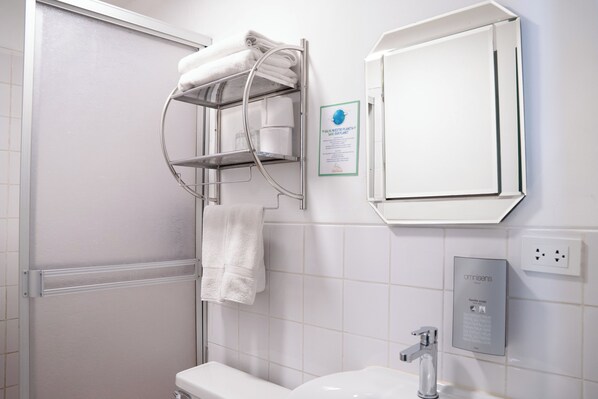 A bathroom with a white sink, a towel rack with folded towels, a mirror, and a wall-mounted electrical outlet.