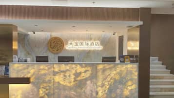 A reception desk with a marble design, a round emblem, and a staircase leading to an upper level.