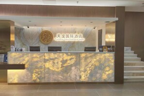 A reception desk with a marble design, a round emblem, and a staircase leading to an upper level.