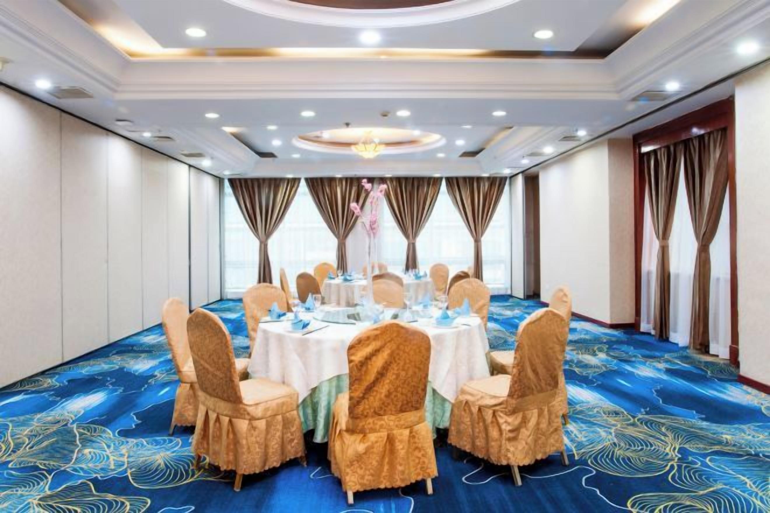 Un salón de conferencias con una mesa redonda, sillas y una alfombra azul con motivos florales.