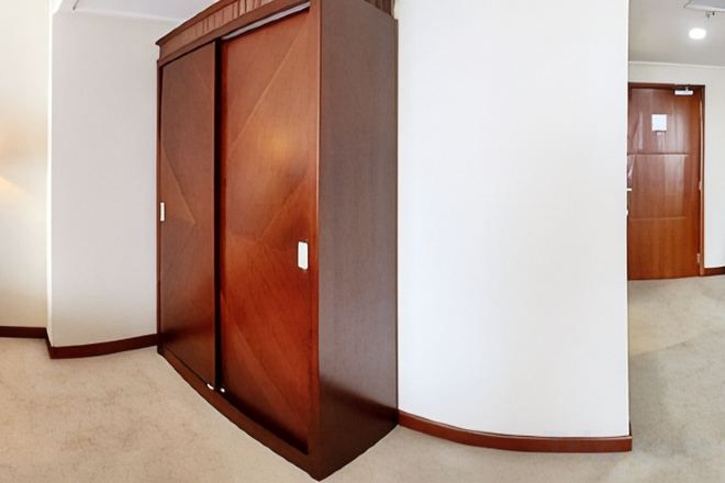 A corner of a room with a wooden wardrobe and a white wall.