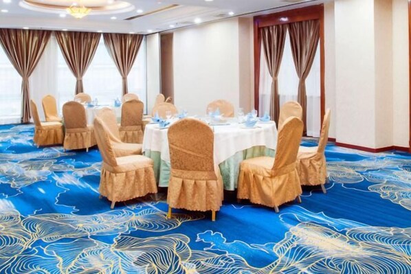 A conference room with round tables and chairs, a blue carpet with a pattern, and curtains on the windows.
