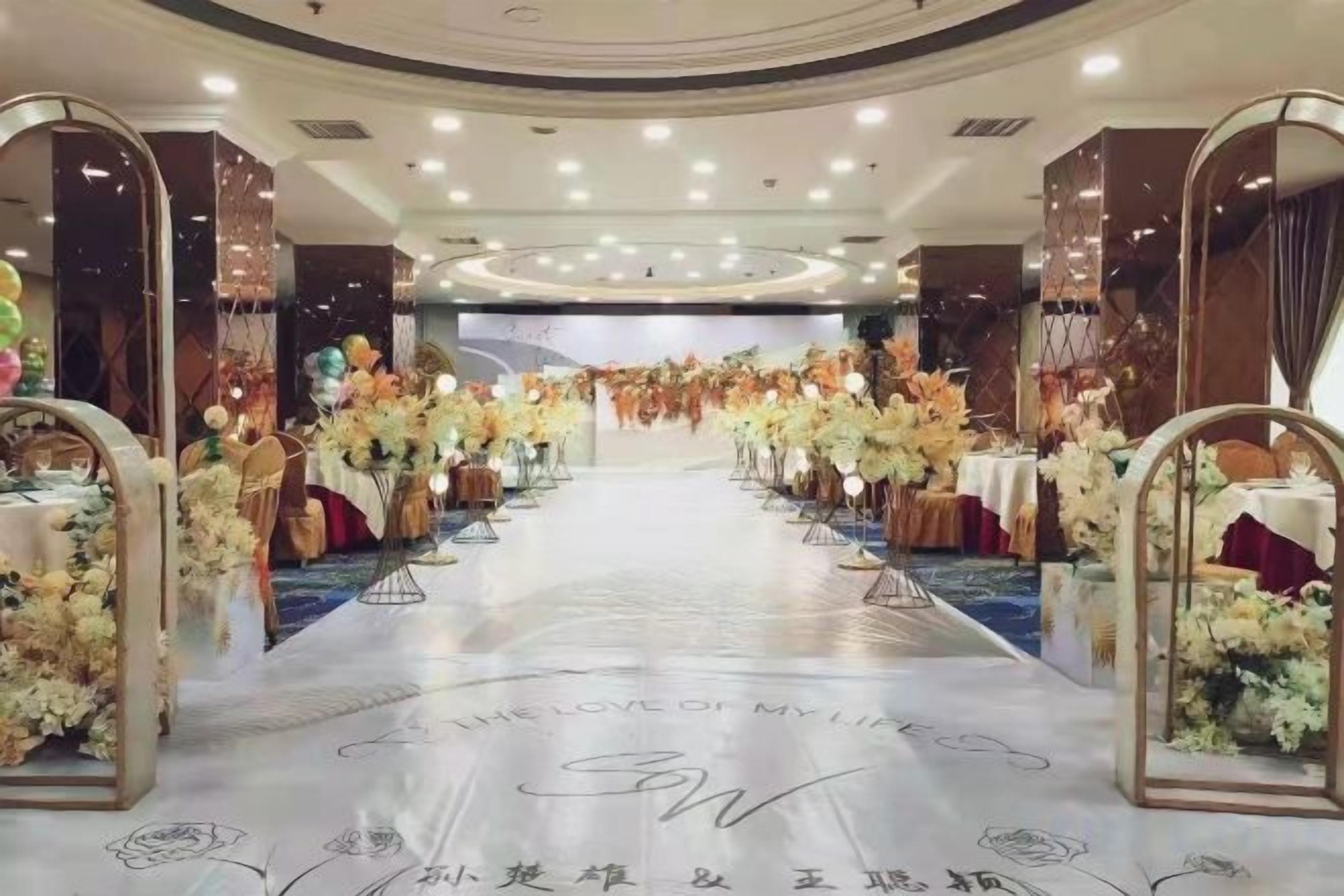 A banquet hall with a central aisle, tables on either side, and floral decorations.