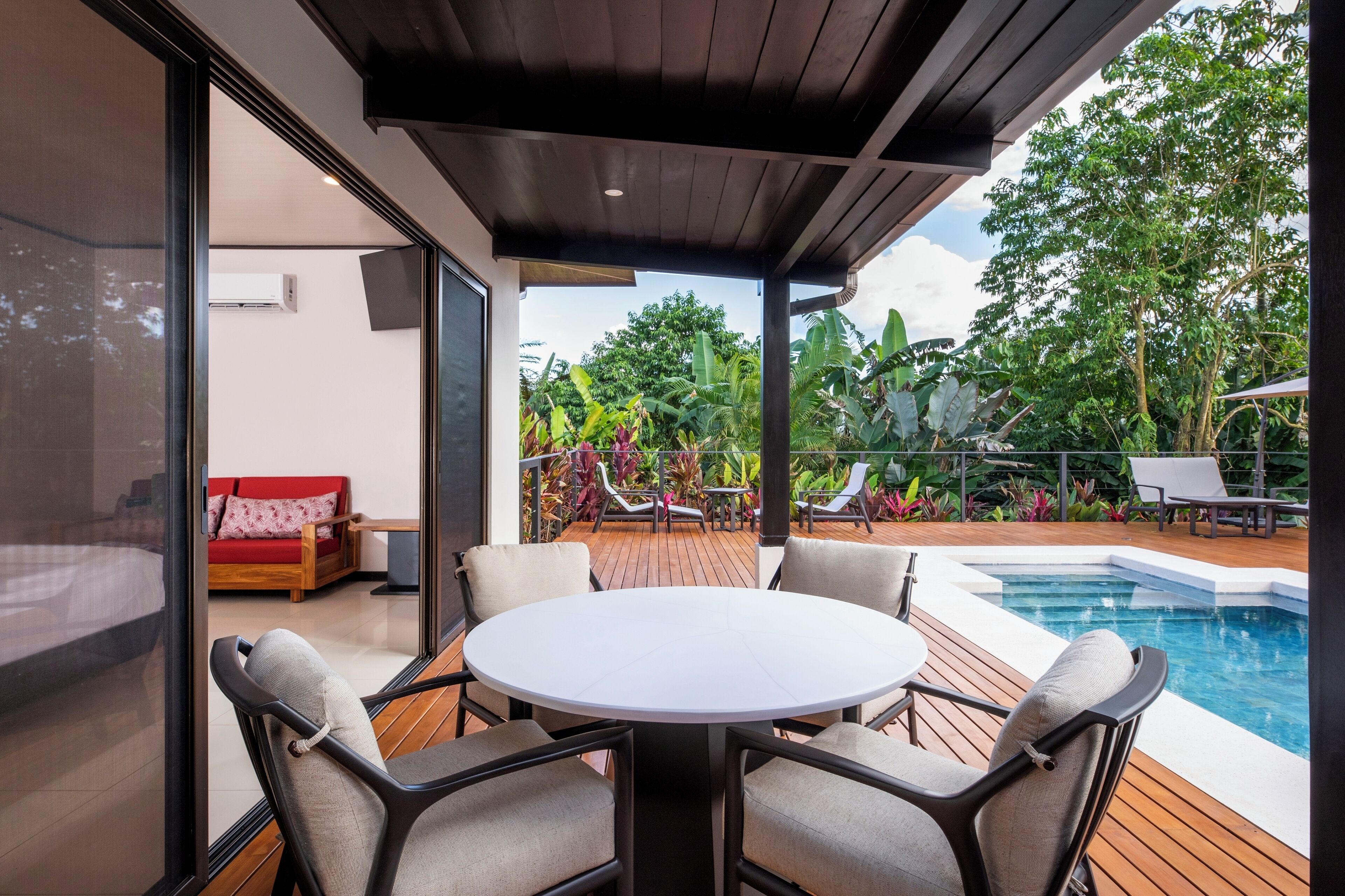 A modern outdoor patio with a pool, surrounded by lush greenery and a wooden deck.