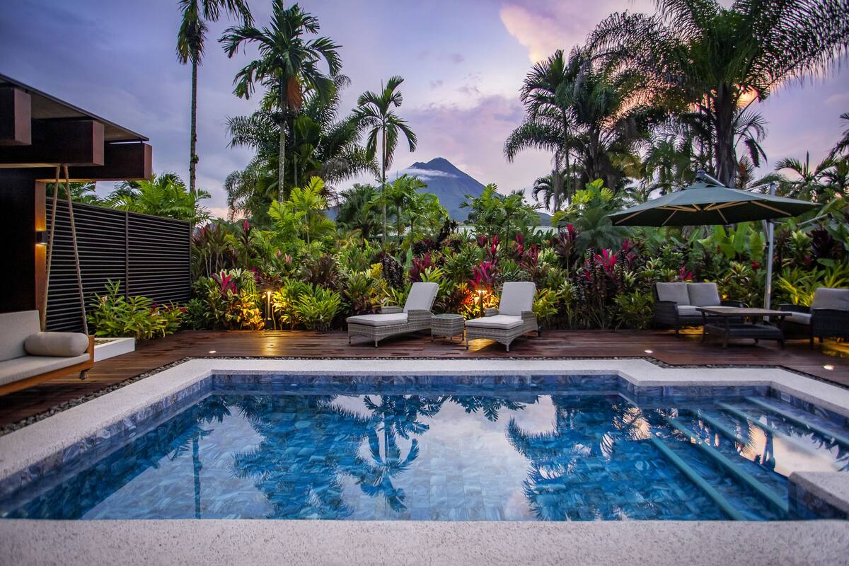 A pool area with lounge chairs, a wooden deck, and tropical plants.