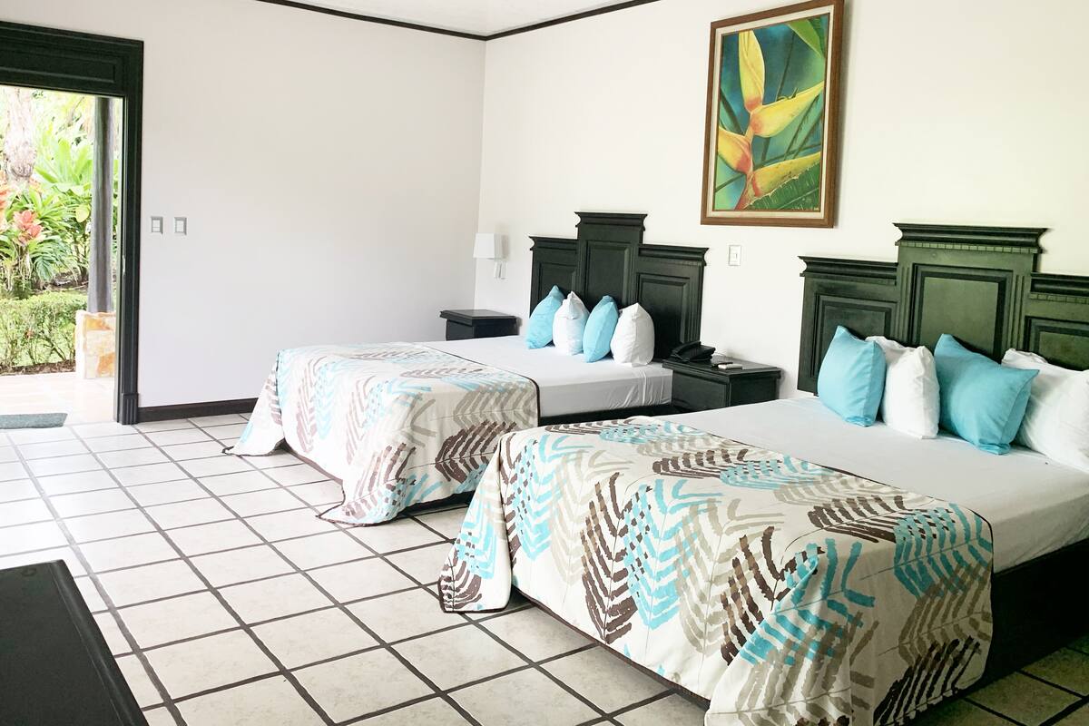A hotel room with two beds, a large window, and a painting on the wall.