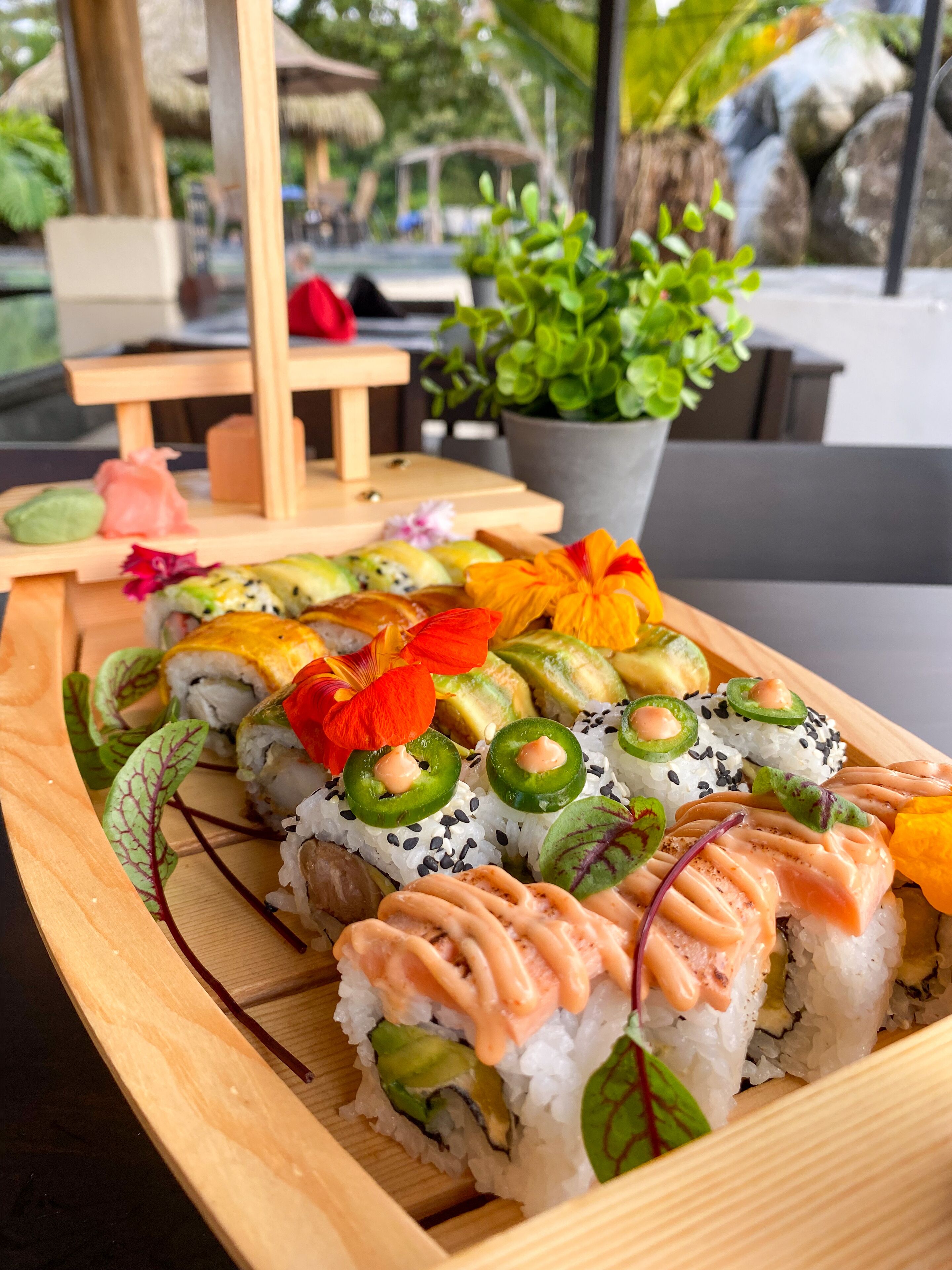 Un plato de madera con sushi variado, incluyendo rollos de aguacate y salmón, dispuesto sobre una mesa.