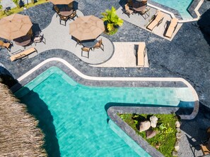 A pool area with lounge chairs and umbrellas, surrounded by a stone deck. - Arenal Manoa & Hot Springs Resort (La Fortuna)