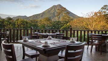A restaurant with outdoor seating, tables set for dining, and a mountain view.