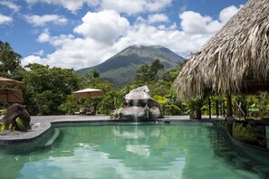 A pool with a waterfall feature, surrounded by tropical vegetation and a thatched-roof structure. - Arenal Manoa & Hot Springs Resort (La Fortuna)