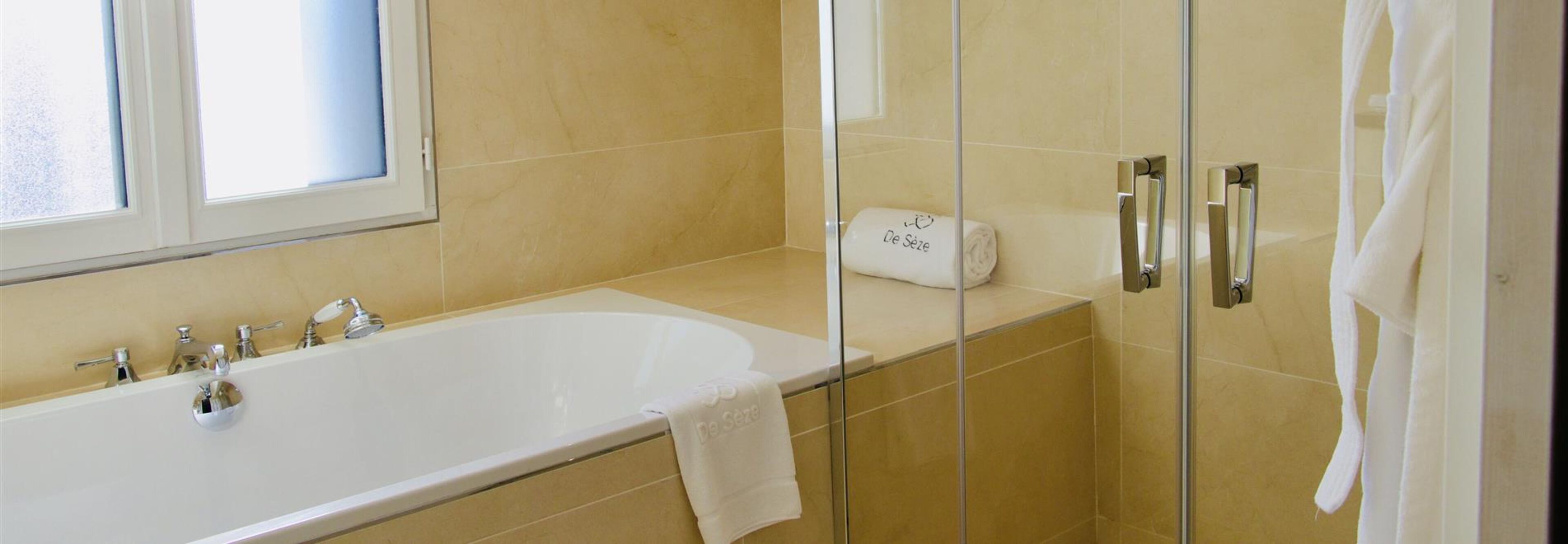 Un baño moderno con una bañera amplia, cabina de ducha con mampara de vidrio y ventana que proporciona luz natural.