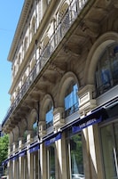Un edificio con diversi balconi, ampie finestre e un tendone blu con la scritta 'Semaine'.
