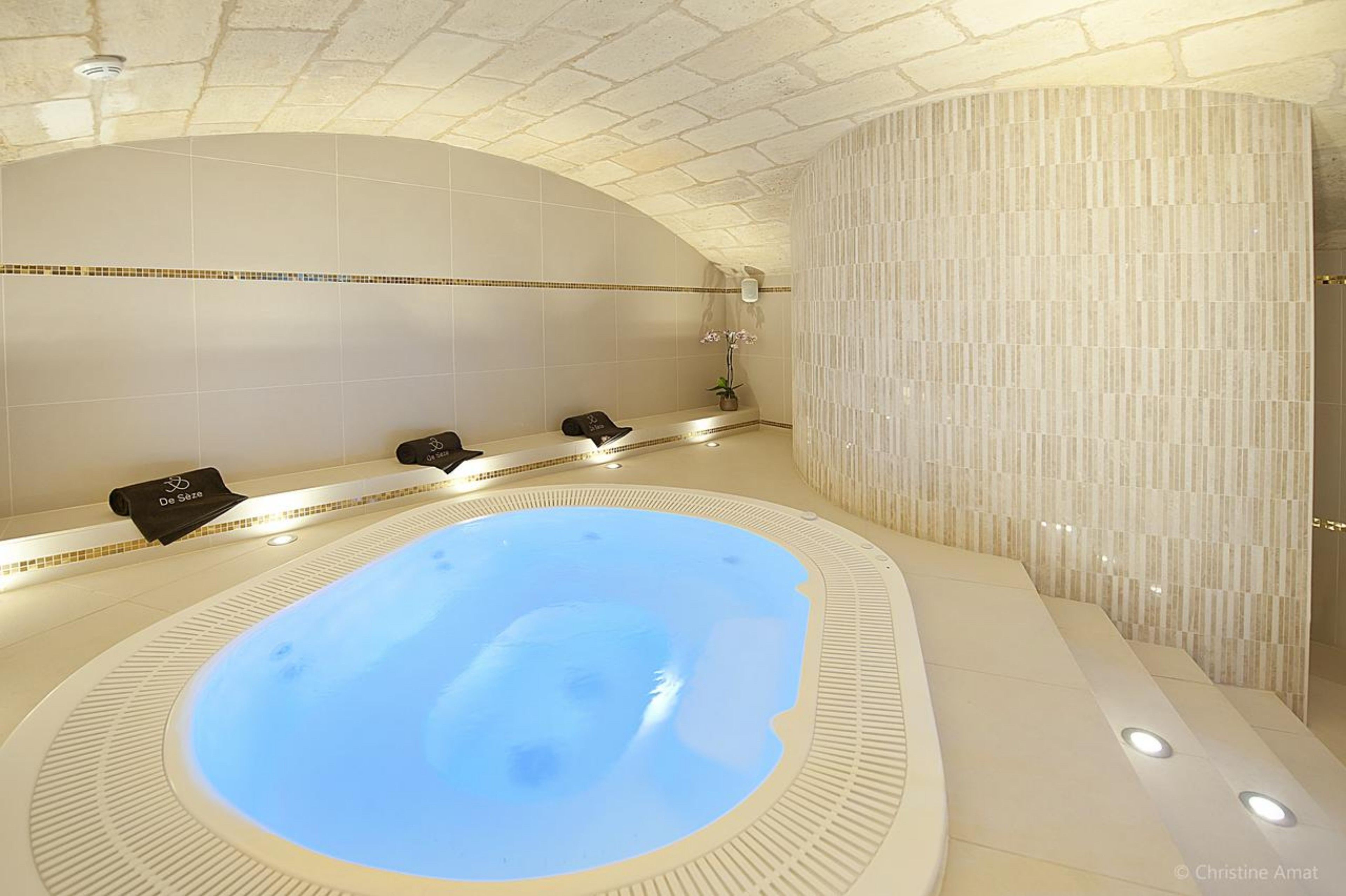 A spa area with a large hot tub, a seating area with towels, and a wall with a textured pattern.