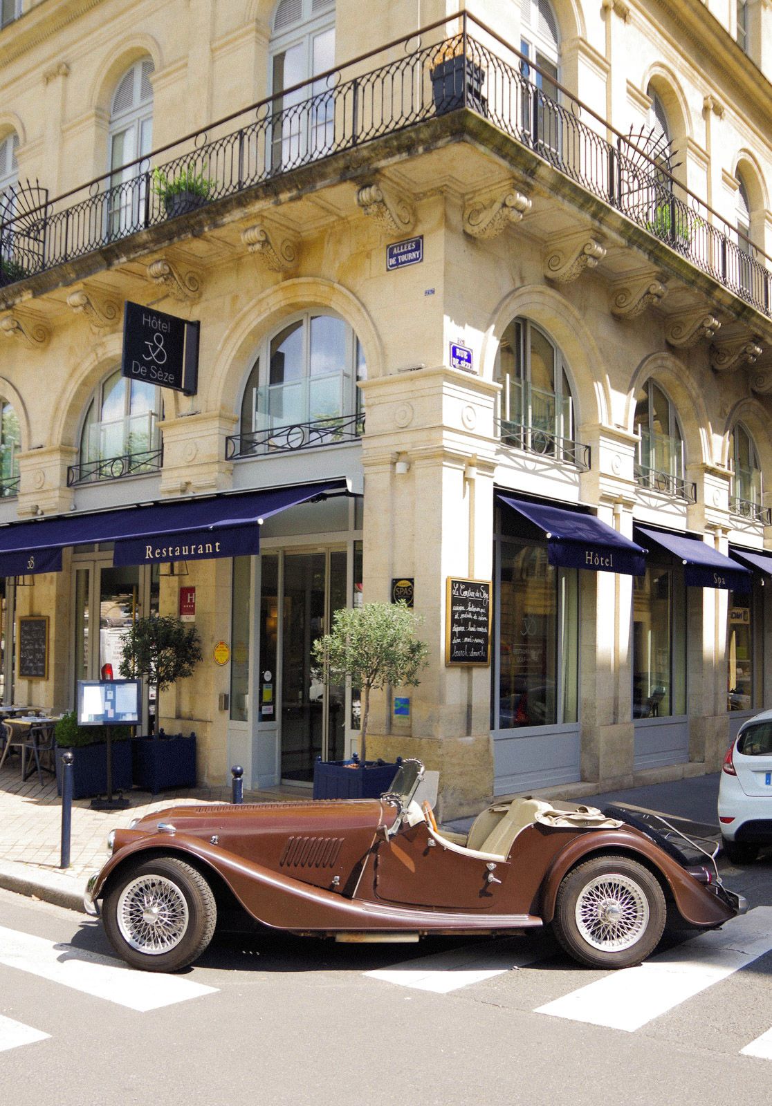 Un coche convertible antiguo estacionado frente a un edificio con un letrero que dice 'Hotel De Seze'.