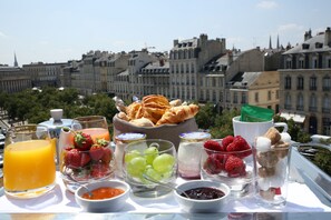 A breakfast spread with various fruits, pastries, and beverages on a table with a city view in the background. - Hôtel de Sèze (Bordeaux)