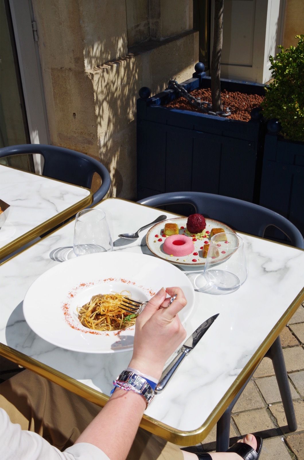 An outdoor dining table with a plate of food, a glass of water, and a dessert.