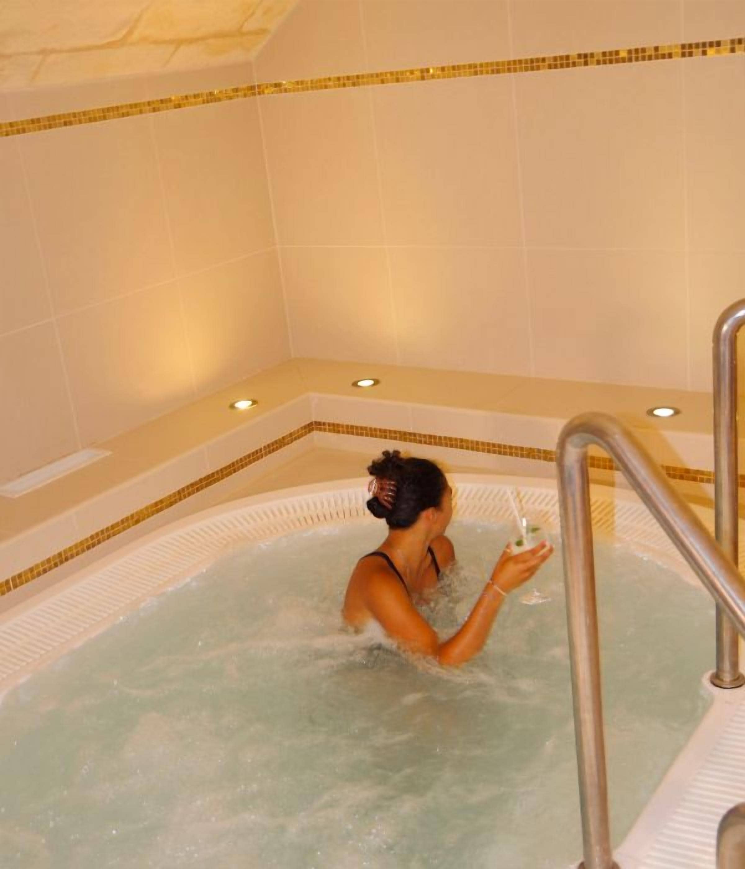 Una persona en un jacuzzi con pared de azulejos y un pequeño borde con luces.