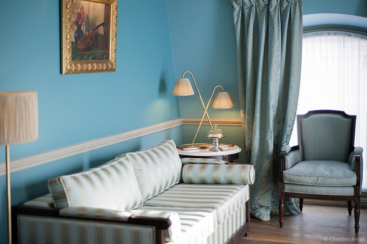 A room with a striped sofa, a chair, a table with lamps, and a painting on the wall.