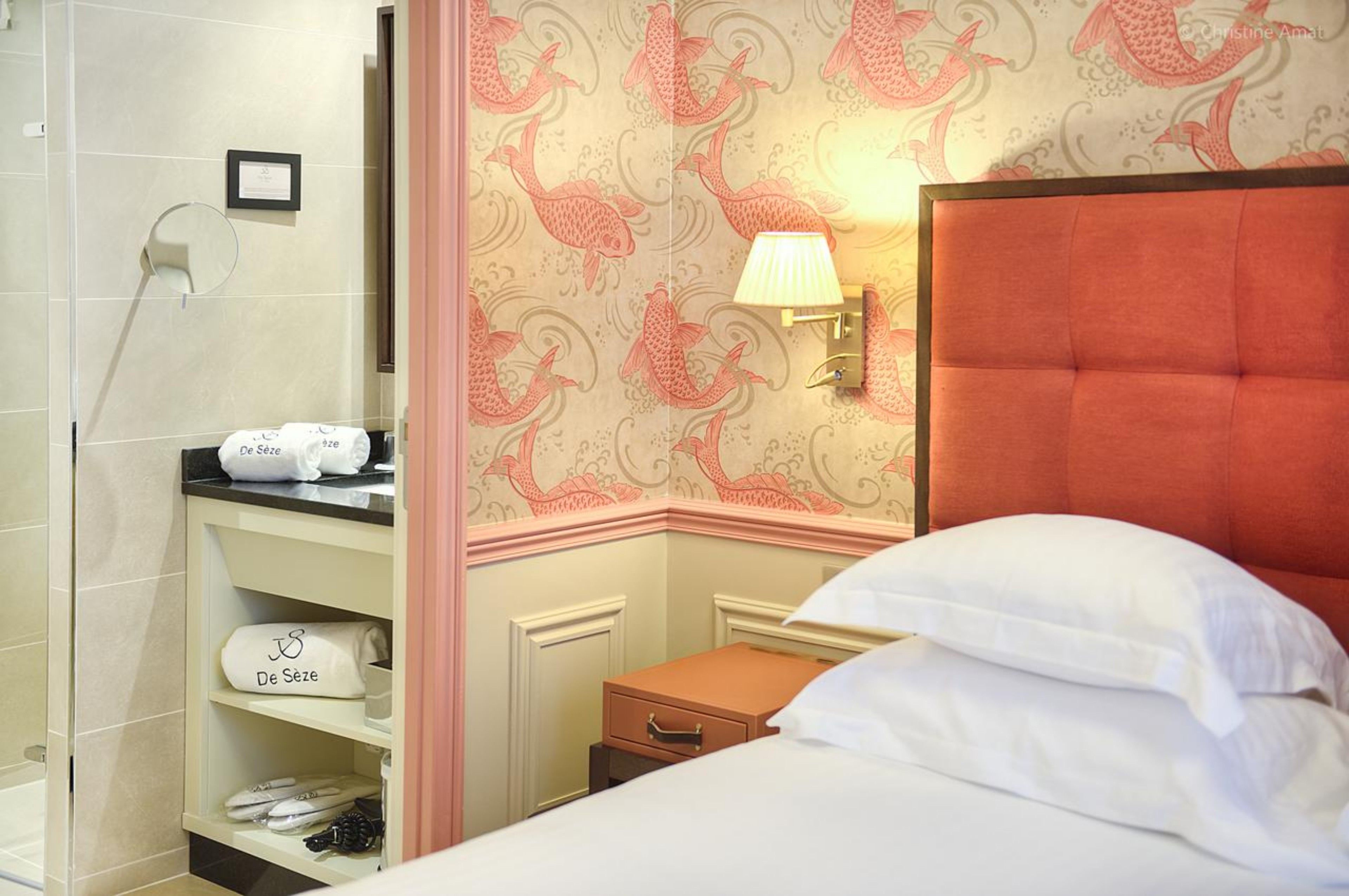 Une chambre d’hôtel avec un lit, une table de chevet, un porte-serviettes et un mur décoré d’un motif de poissons.