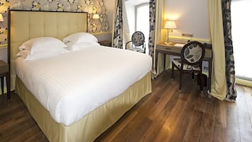Une chambre d’hôtel avec un grand lit, un bureau avec une chaise, une lampe et une fenêtre avec des rideaux.