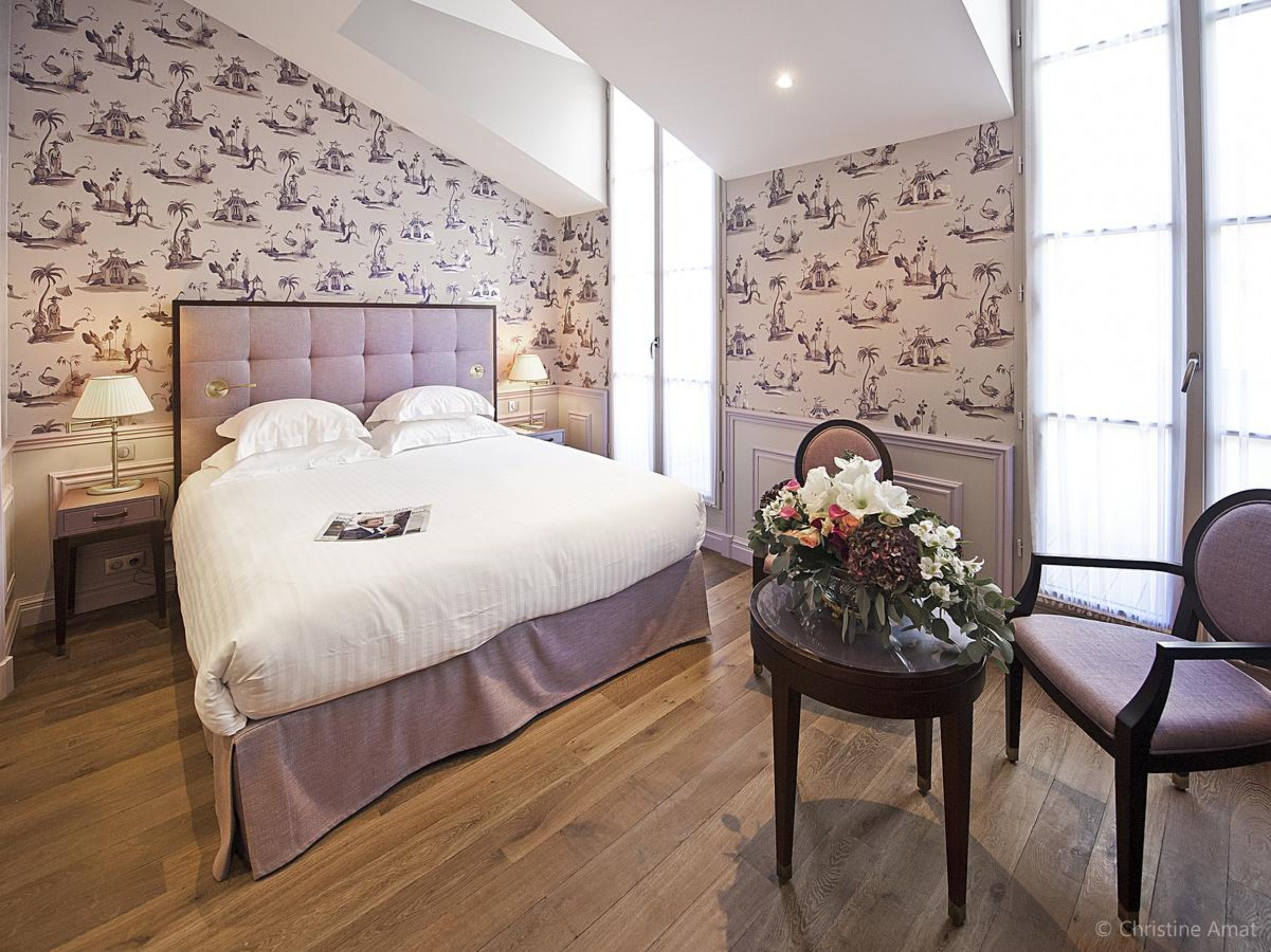 Un dormitorio con una cama grande, una mesita de noche, una silla, una mesa con flores y una ventana con vistas.