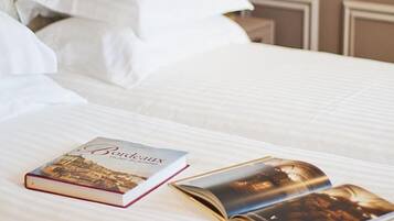 A neatly made bed with white linens, a book titled 'Bordeaux', and a lamp on a bedside table.