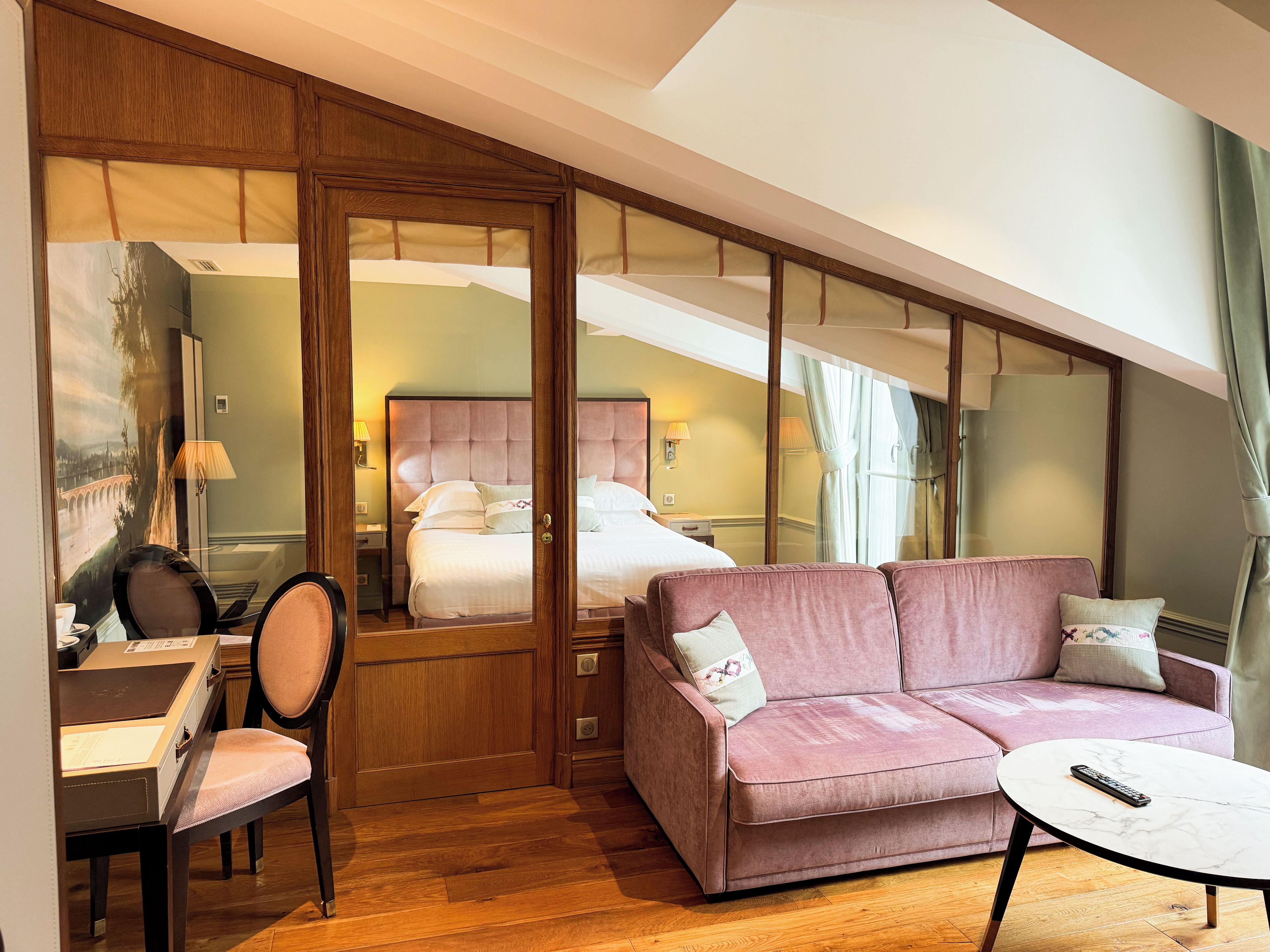 A hotel room with a bed, a sofa, a desk with a chair, and a small table.