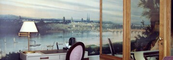 A room with a desk, a lamp, and a large window with a cityscape mural.